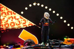 Max Verstappen stojí v kombinéze Red Bull na svém voze F1 po vítězném sprintu. V pozadí je dramatické pódiové osvětlení.