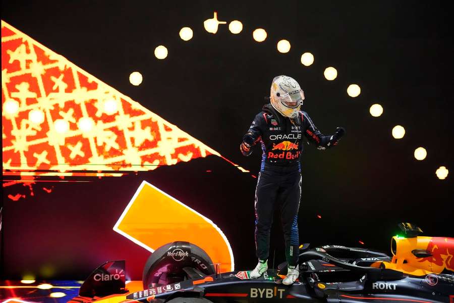 Max Verstappen stojí v kombinéze Red Bull na svém voze F1 po vítězném sprintu. V pozadí je dramatické pódiové osvětlení.