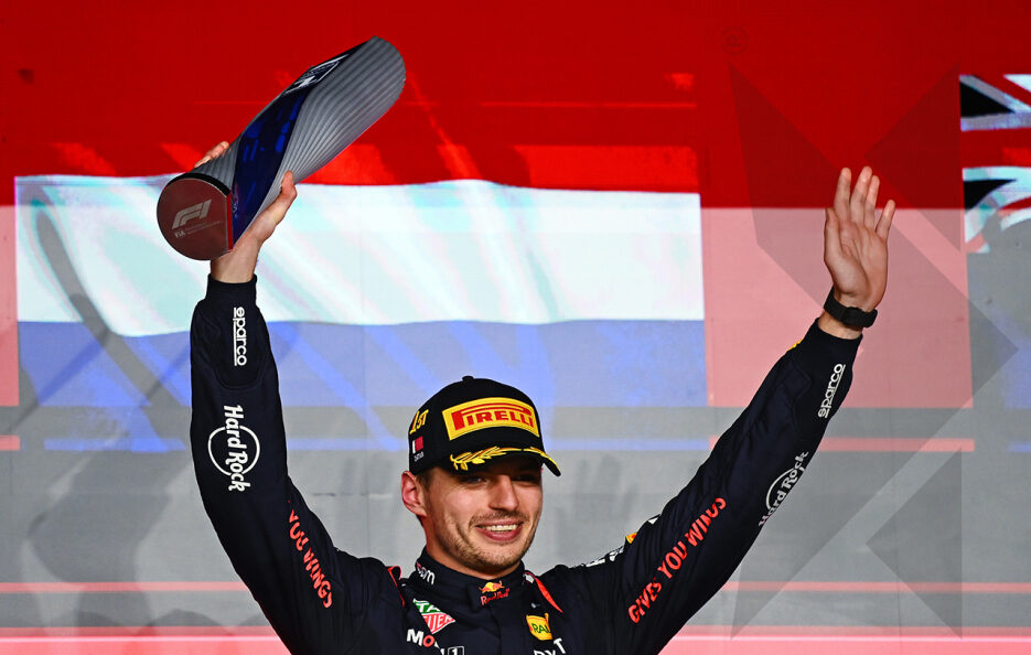 Max Verstappen slaví vítězství ve Velké ceně Kataru na stupních vítězů s pohárem a zvednutými pažemi.
